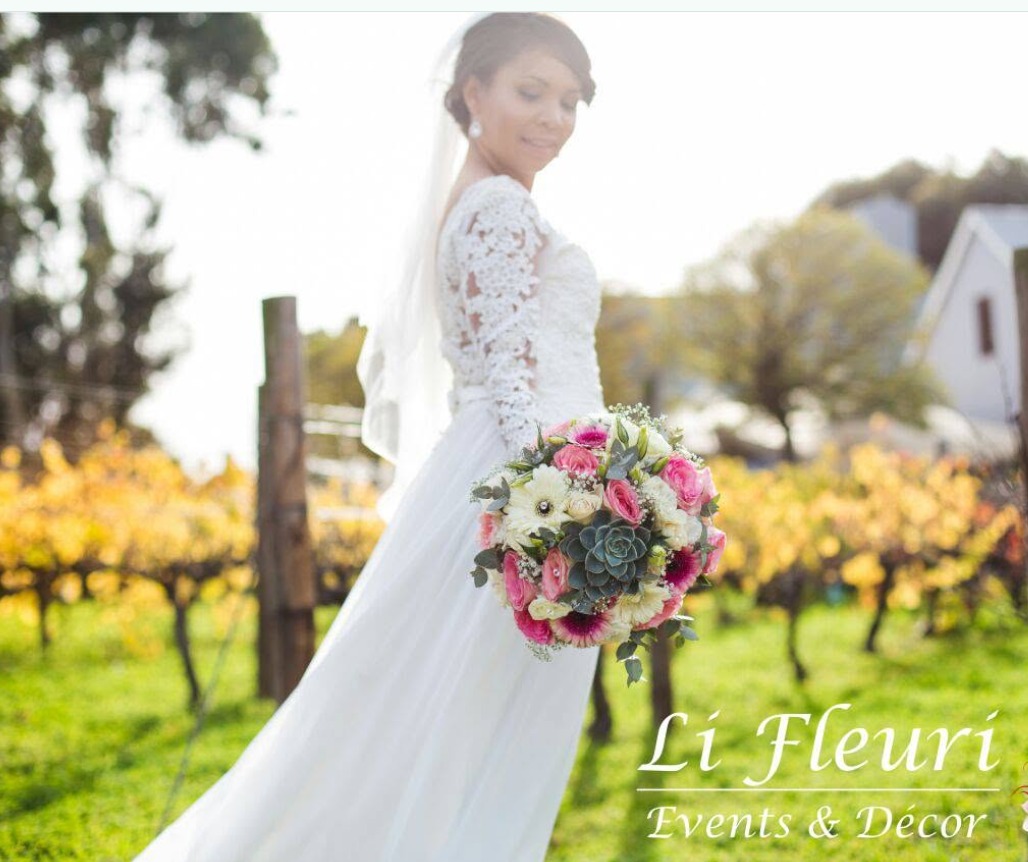 Bride in a lace gown holding a pink and white bouquet in a vineyard