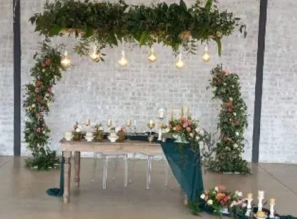 Head table framed by a hanging greenery installation, floral garlands and warm lights