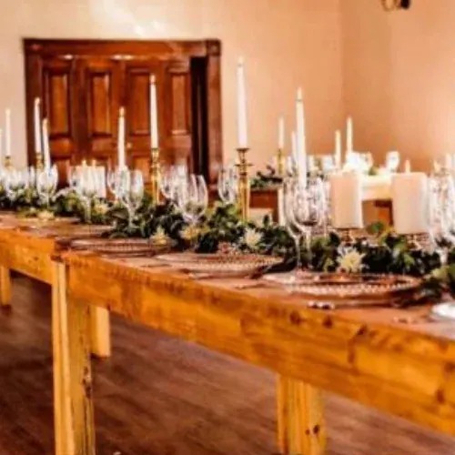 Wooden reception table with a greenery runner, white flowers and tall white candles