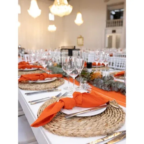 Reception table with burnt orange napkins, woven placemats and greenery