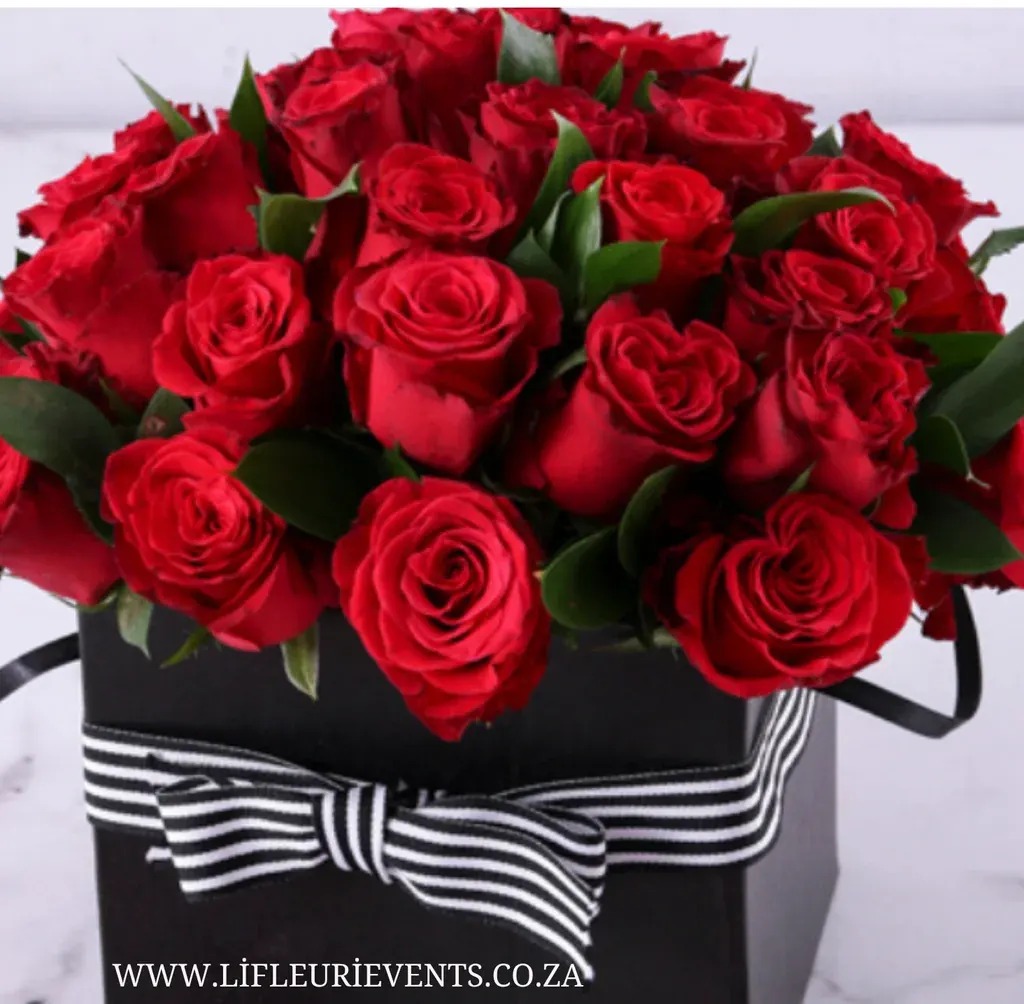 Red roses and greenery arranged in a black box with a striped ribbon