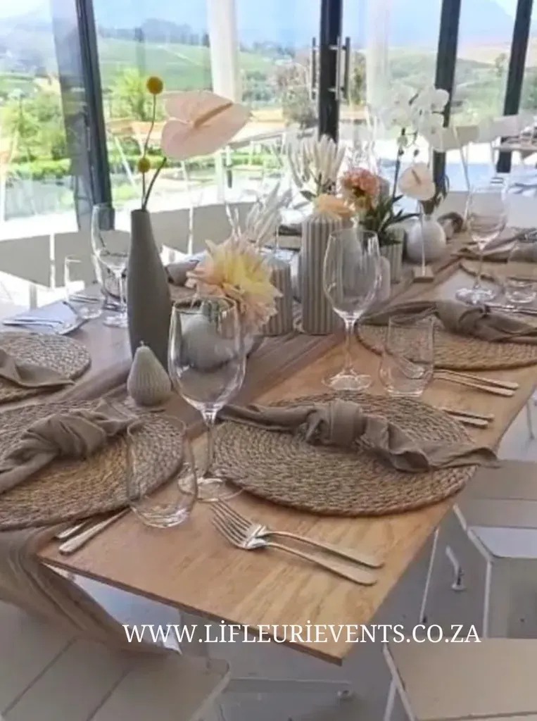 Wooden reception table with white floral bud vases, woven placemats and glassware