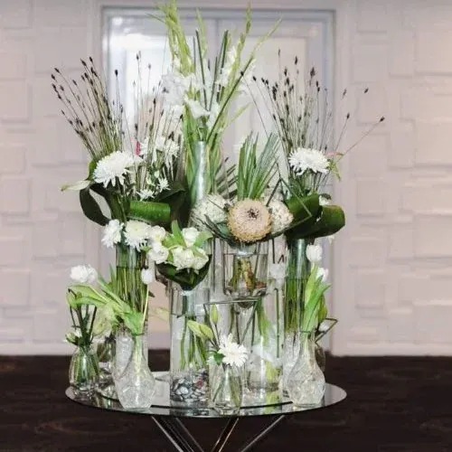 Cluster of glass vases with white flowers, proteas and tall green leaves