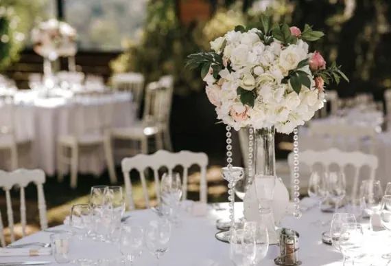 White rose and pink flower arrangement on a tall pedestal above a reception table