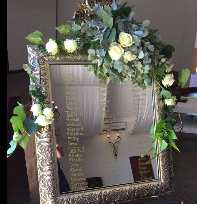 Ornate wedding welcome mirror decorated with white flowers and greenery