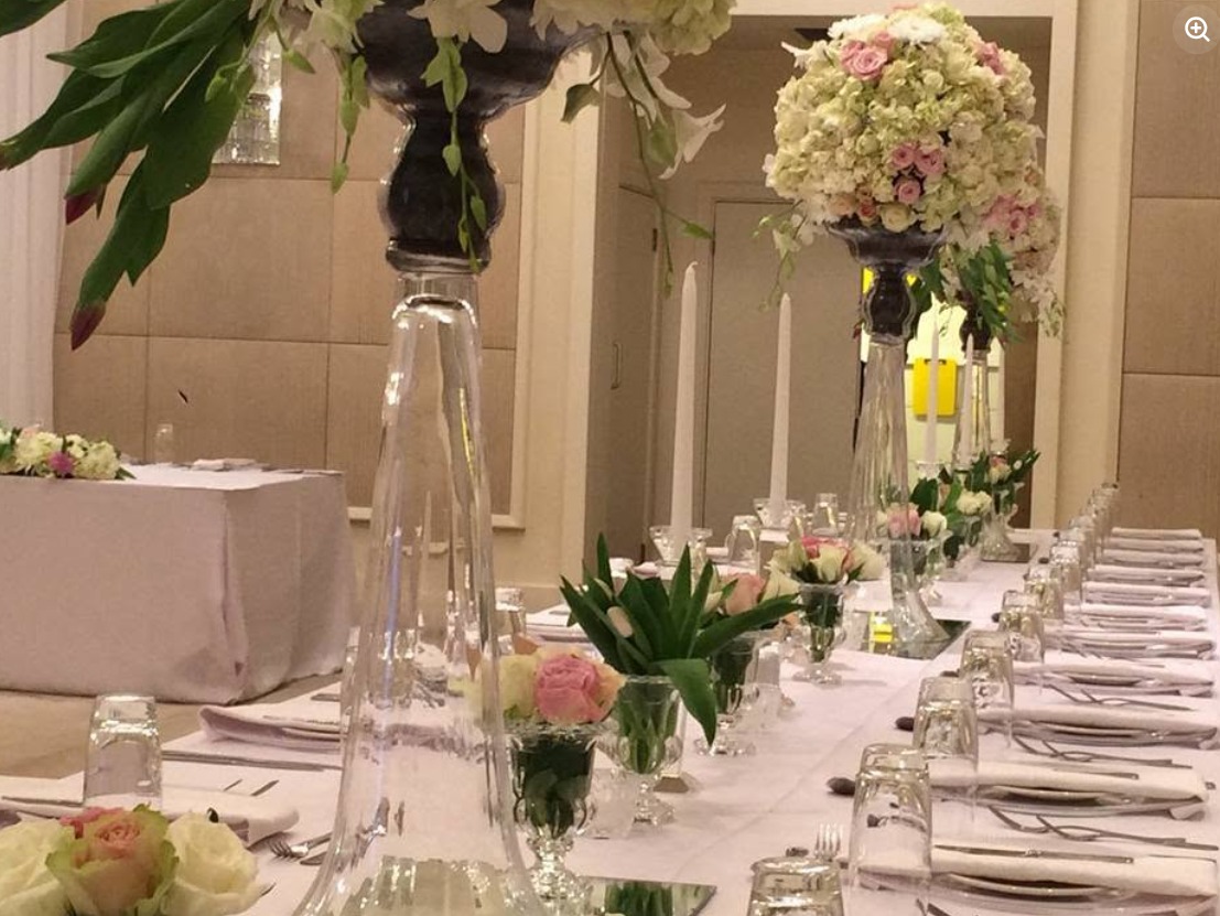 Reception tables with tall glass vase centrepieces of pink flowers and greenery